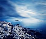 Sea with Rocky Shore at Night. Smooth Water and Clouds. Long Exposure. Toned Photo with Copy Space.