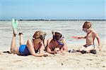 Mother, father and little son on summer vacation at the seaside, They wearing snorkels and flippers while lying and playing on the beach