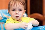 Astonished little boy wearing yellow t-shirt at home, face got dirty with yoghurt