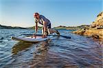 male paddler starting stand up paddling on a rocky shore of Horsetooth Reservoir, Fort Collins, Colorado, summer scenery