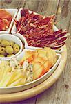 Spanish Snacks with Various Cheeses, Jamon, Cured Ham and Green Olives on Serving Plate closeup on Wooden background. Retro Styled