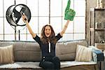 Portrait of happy young football fan woman watching tv in loft apartment and rejoicing. Urban chic loft decoration details and window. Modern lifestyle concept.