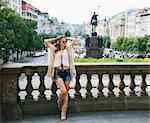 Portrait of hippy-looking woman tourist relaxing near stone parapet in the historical center of Prague. In the background Saint Wenceslas statue on Wenceslas Square in Prague. Tourism travel concept.