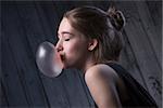 Portrait of sexual brown-haired, which inflates languidly pink bubble of chewing gum. Photographed in studio on a dark background.