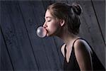 Portrait of sexual brown-haired, which inflates languidly pink bubble of chewing gum. Photographed in studio on a dark background.