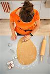 Housewife cutting out Halloween biscuits with pastry cutter from rolled pastry in kitchen. Traditional autumn holiday. Upper view
