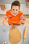 Cheerful young woman holding cookie cutters for Halloween biscuits in kitchen. Traditional autumn holiday. Upper view