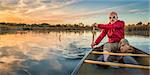 senior paddler enjoying paddling a canoe on a calm lake at sunset, Riverbend Ponds Natural Area, Fort Collins, Colorado