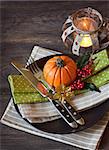 Festive autumn place settings with pumpkin, berries and candle on wooden background.