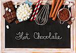 Hot chocolate mix on old chalk blackboard. Sweet marshmallow, chocolate bars, sugar, cocoa powder, cinnamon, and whisk for cooking winter holiday drink.