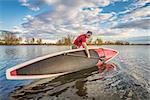 senior male launching  his 14 feet long expedition stand up paddleboard on a lake in Colorado, fall scenery