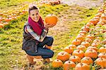 Portrait of beautiful smiling woman next to rows of pumpkins and choosing pumpkin on pumpkin patch on farm during the autumn season