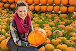 Portrait of smiling woman sitting and holding big pumpkin on farm during the autumn season