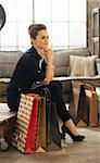 Dreamy brown-haired elegant woman with shopping bags relaxing after great shopping in stylish loft apartment. Luxurious life concept