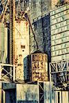 industrial background with grunge texture effect - exterior of old abandoned grain elevator with pipes, ducts, ladders and chutes
