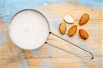 almond milk in measuring cup with almond nuts against wooden background