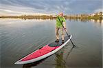 senior male paddler on a paddleboard, lake in Colorado with a fall scenery and dark clouds