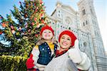 Smiling mother and daughter showing thumbs up in front of Christmas tree near Duomo in Florence, Italy. Modern family enjoying carousel of Christmas time events in heart of the Renaissance.