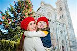 Smiling mother and daughter hugging in front of Christmas tree near Duomo in Florence, Italy. Modern family enjoying carousel of Christmas time events in heart of the Renaissance.