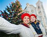 Happy mother and daughter taking selfie in front of Christmas tree near Duomo in Florence, Italy. Modern family enjoying carousel of Christmas time events in heart of the Renaissance.
