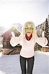 Going wild for Christmas season in a secluded spot in the countryside. Smiling young woman in funny Christmas tree glasses showing thumbs up in the front of a cosy mountain house.