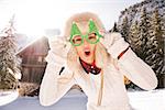 Going wild for Christmas season in a secluded spot in the countryside. Portrait of merry young woman in funny Christmas tree glasses having fun in the front of a cosy mountain house.