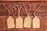 four blank paper price tags with a twine against a rustic scratched wood