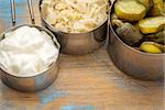 sauerkraut, cucumber pickles and yogurt - popular probiotic fermented food - three measuring cups against rustic wood