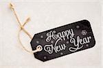 HappY new Year on a black  price tag with a twine against a ceramic tile background
