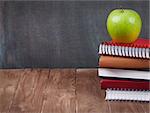 School and office supplies and apple on classroom table in front of blackboard. View with copy space