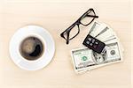 Money cash, glasses, car remote and coffee cup on wooden table