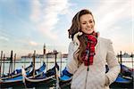 Sunset brings to life irresistible magic of Venice - the unique Italian city. Happy and dreamy young woman traveler standing on embankment in the front of the line of gondolas