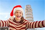 Young, itching from energy and searching for excitement. I'm going to Christmas trip to Italy. It is a no-brainer. Happy woman in Santa hat taking selfie in front of Leaning Tour of Pisa.