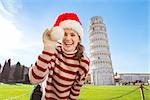 Young, itching from energy and searching for excitement. I'm going to Christmas trip to Italy. It is a no-brainer. Happy woman playing with Santa hat in front of Leaning Tour of Pisa.