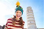 Young, itching from energy and searching for excitement. I'm going to Christmas trip to Italy. It is a no-brainer. Portrait of happy woman in Christmas tree hat in front of Leaning Tour of Pisa