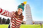 Young, itching from energy and searching for excitement. I'm going to Christmas trip to Italy. It is a no-brainer. Happy woman in Christmas tree hat taking selfie in front of Leaning Tour of Pisa