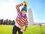 Young, itching from energy and searching for excitement. I'm going to Christmas trip to Italy. It is a no-brainer. Smiling woman make fun of Christmas tree hat in front of Leaning Tour of Pisa