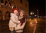 Holiday family trip to Venice, Italy can change the whole Christmas experience. Portrait of happy mother and child standing on Piazza San Marco in the evening. Winter Tourism
