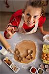 Christmas season can inspire you in the kitchen and you may want to treat your family with edible gifts. Modern young housewife showing cookie cutter. She is making Christmas themed cookies