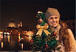 Tune in for charming Christmas time in Venice, Italy. Happy young woman with a Christmas tree standing on a bridge overlooking Grand canal and looking into distance