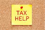 Tax Help written on yellow sticky note pinned with red push pin on cork board.