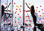 Mixed race secretary working in modern office in skyscraper, sticking adhesive notes with tasks on window. The girl feels stressed and overwhelmed