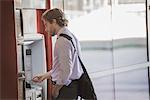 A man with a laptop bag using an ATM, a cash machine on a city street.