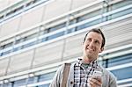 A man in a checked shirt with open collar holding his smart phone.