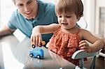 A man and a young child sitting playing with toy cars.