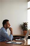 Singapore, Businessman looking up while working at laptop in office