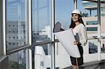 Singapore, Smiling female architect with hardhat and building plans looking through window