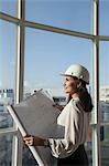 Singapore, Female architect with hardhat and building plans looking through window