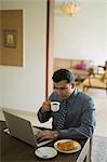 India, Businessman at home with laptop drinking coffee