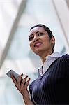 Young woman standing against glass wall with mobile phone in one hand